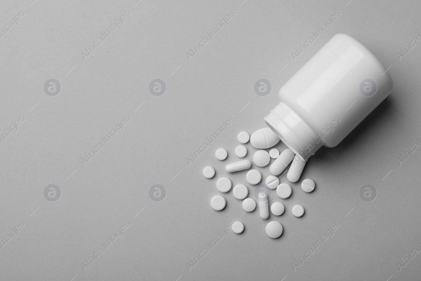 Photo of Bottle with different pills on grey background, flat lay. Space for text