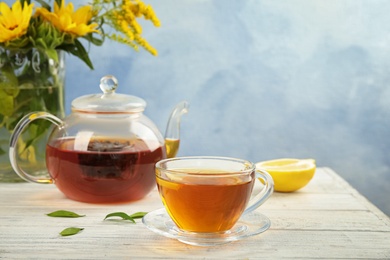 Glass cup and teapot with black tea on wooden table