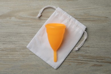 Photo of Menstrual cup with cotton bag on wooden background, top view