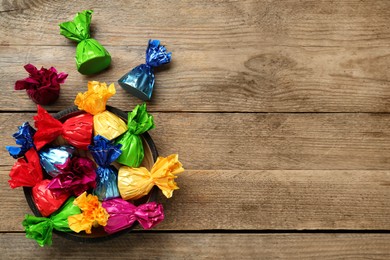 Photo of Candies in colorful wrappers on wooden table, flat lay. Space for text