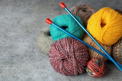 Photo of Soft woolen yarns and knitting needles on grey table, space for text