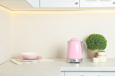 Photo of Modern electric kettle, dishes and houseplant on counter in kitchen