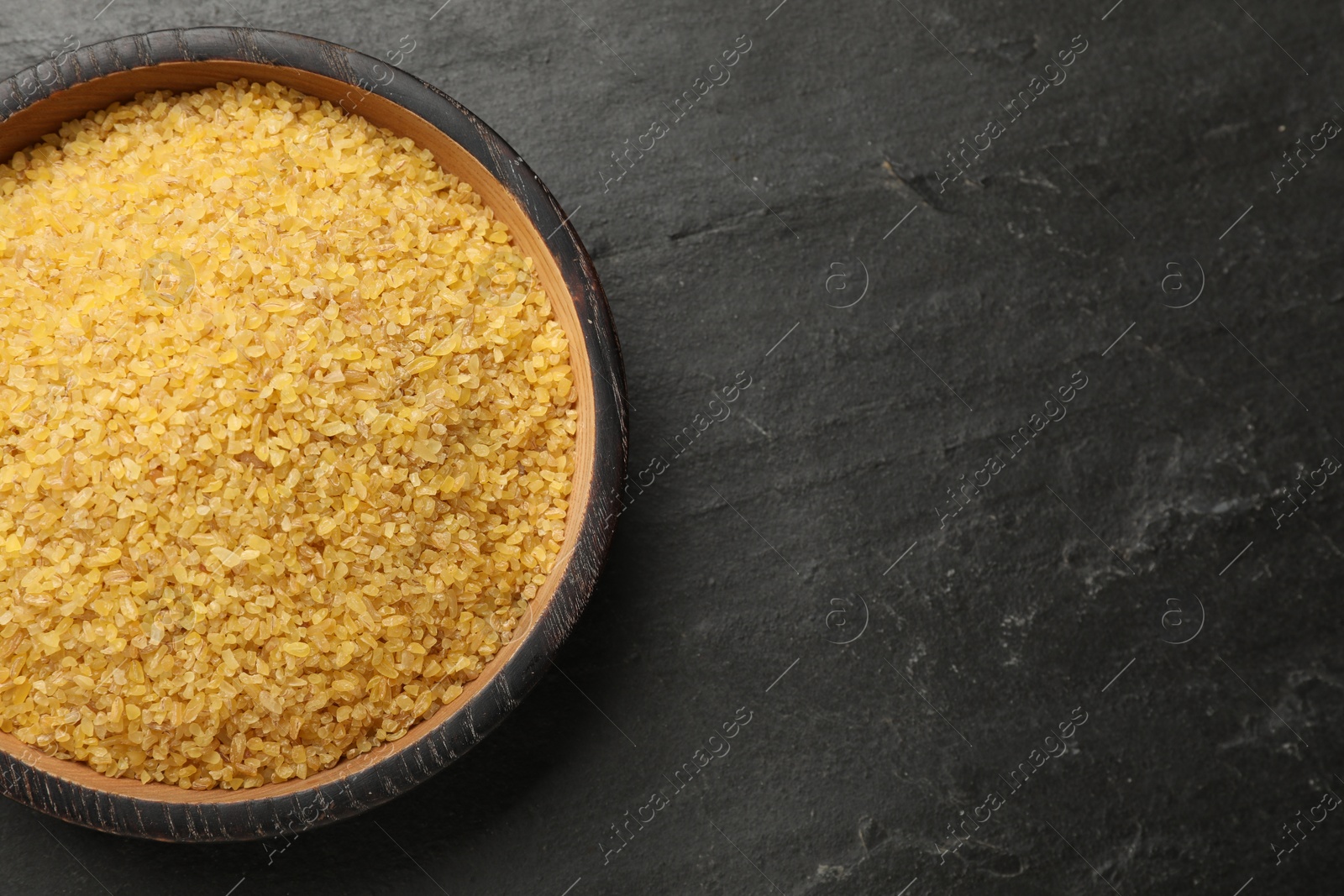 Photo of Raw bulgur in bowl on dark gray table, top view. Space for text