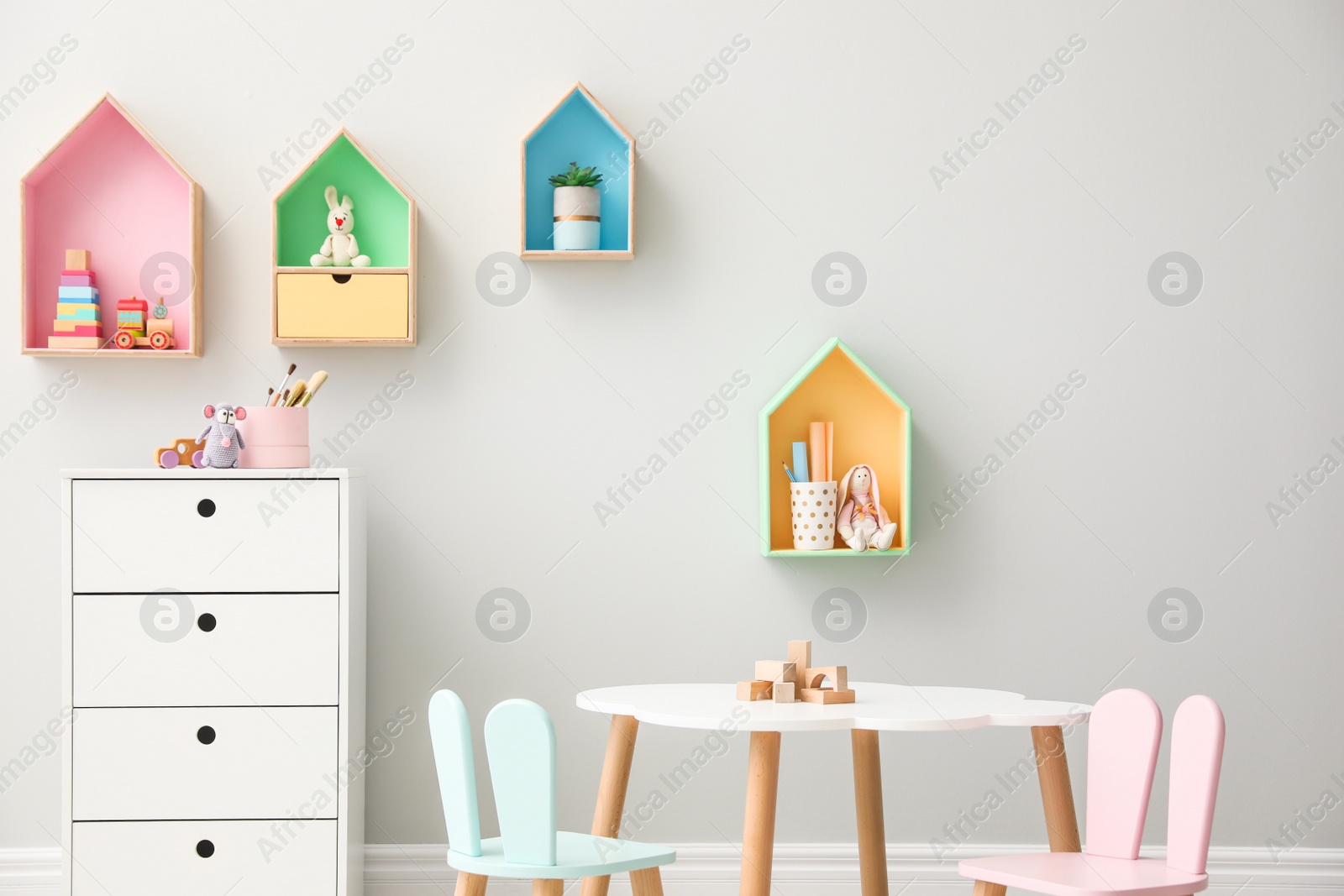 Photo of House shaped shelves and little table with chairs in children's room. Interior design