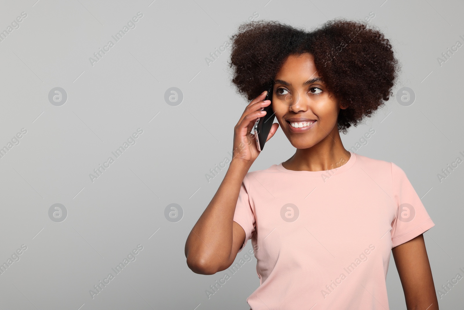 Photo of Smiling African American woman talking on smartphone against light grey background. Space for text