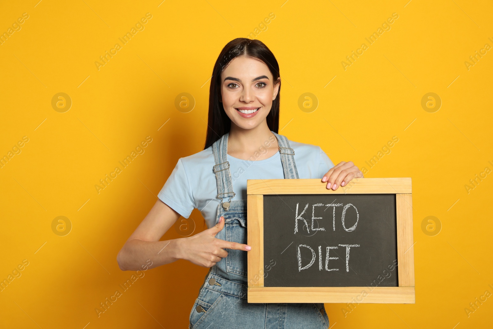 Photo of Happy woman holding chalkboard with words Keto Diet on yellow background