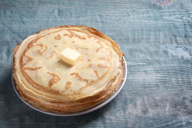 Plate with thin pancakes and butter on wooden table