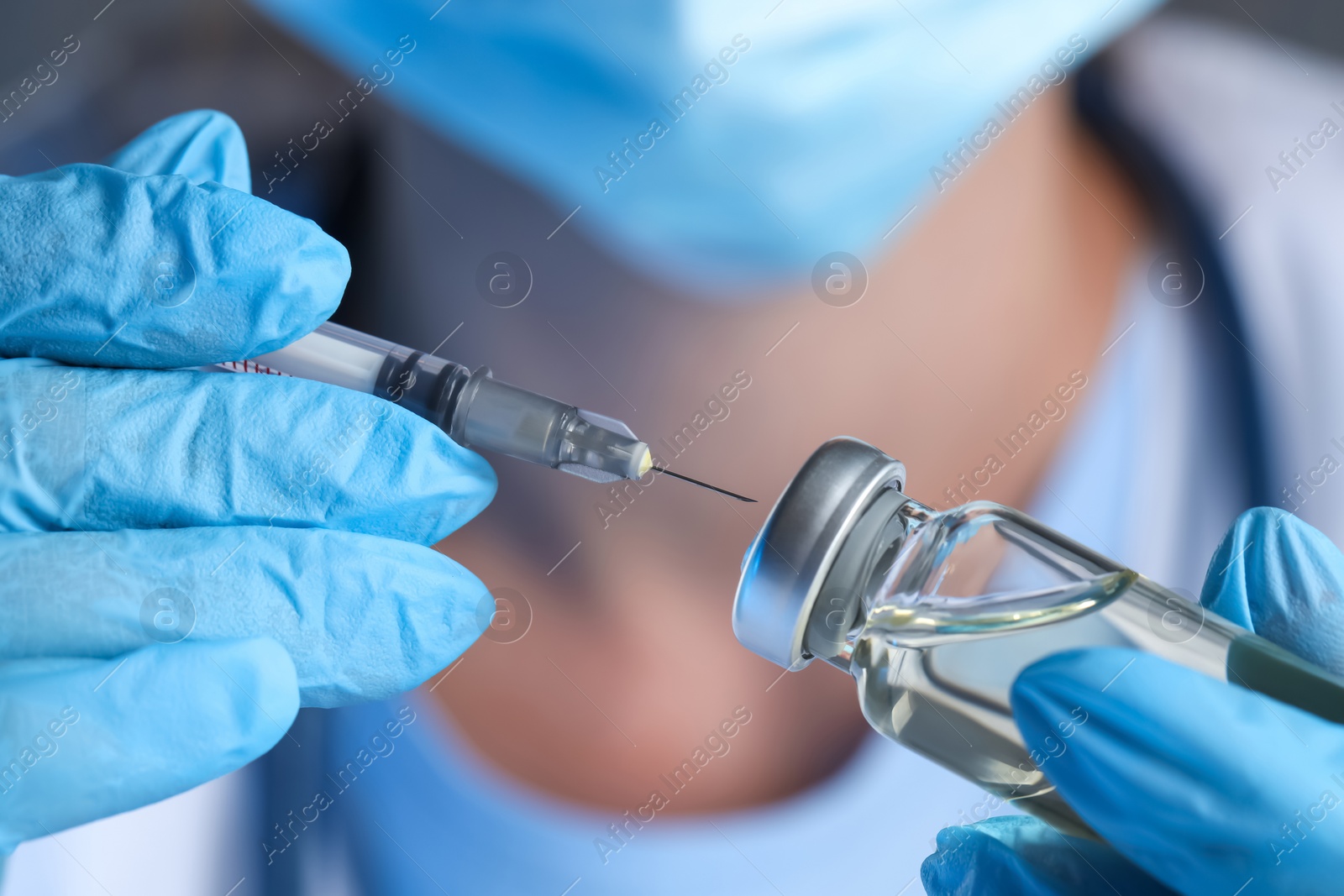 Photo of Doctor inserting syringe into glass vial with medication, closeup