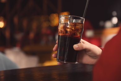 Man holding glass of refreshing cola at table indoors, closeup. Space for text