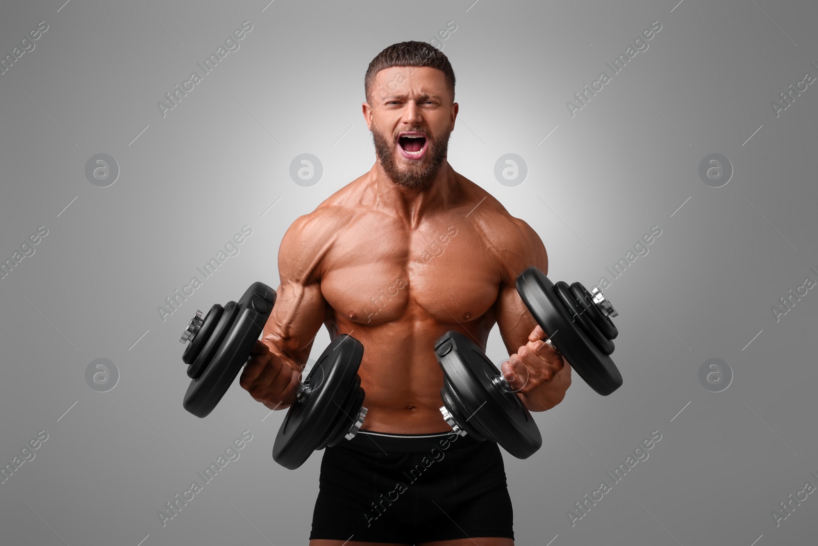 Photo of Emotional young bodybuilder exercising with dumbbells on light grey background