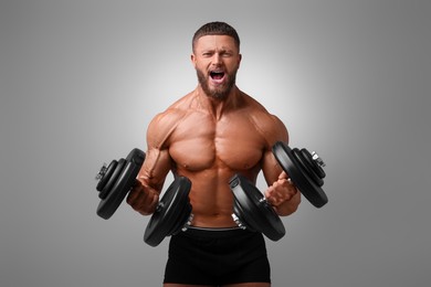 Photo of Emotional young bodybuilder exercising with dumbbells on light grey background