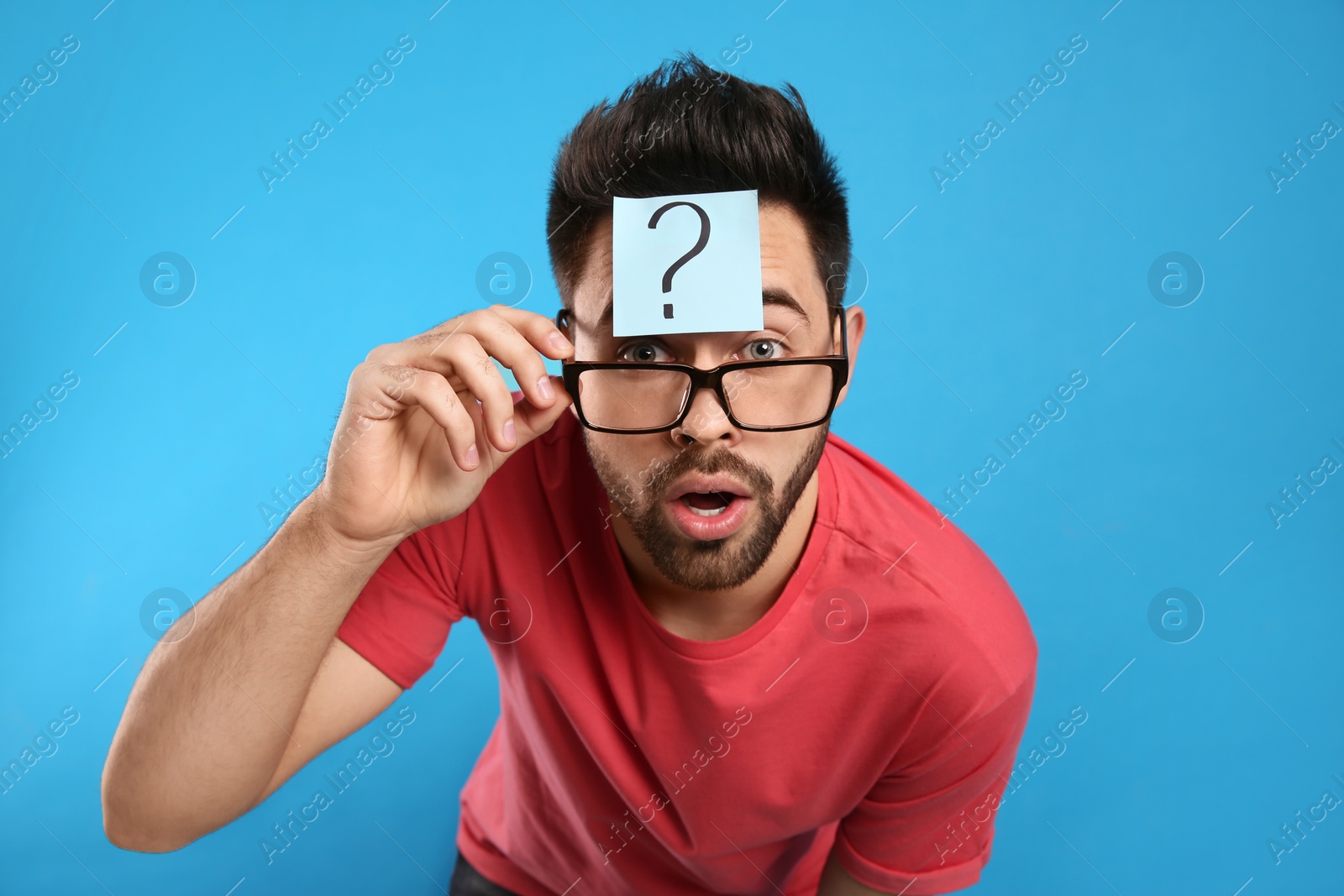 Photo of Emotional young man with question mark sticker on forehead against light blue background