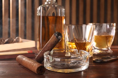 Photo of Cigars, ashtray, whiskey and cutter on wooden table, closeup