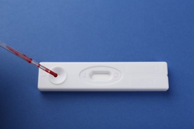 Photo of Dropping blood sample onto disposable express test cassette with pipette on blue background, above view