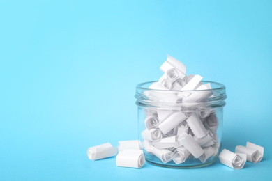 Photo of Glass jar full of rolled paper sheets on light blue background, space for text