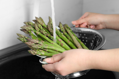 Photo of Woman washing fresh raw asparagus over sink, closeup