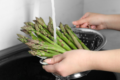 Woman washing fresh raw asparagus over sink, closeup