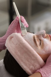 Photo of Cosmetologist applying mask on woman's face in clinic, closeup