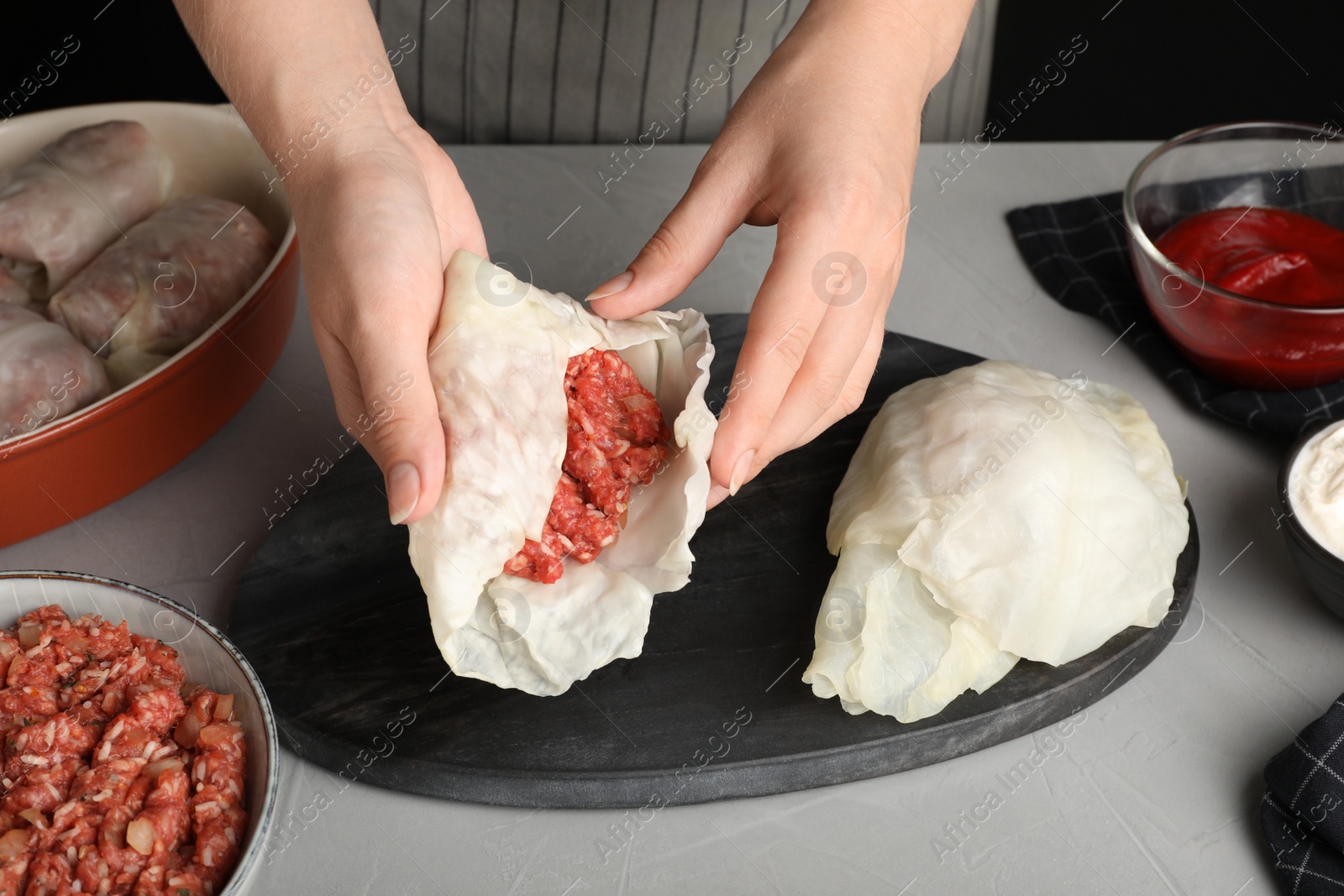 Photo of Woman preparing stuffed cabbage rolls at grey table, closeup