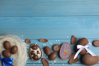 Photo of Flat lay composition with tasty chocolate eggs and candies on blue wooden table, space for text