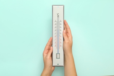 Photo of Woman with weather thermometer on light background, closeup