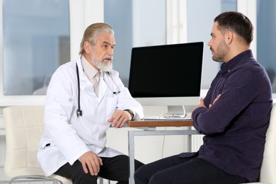Senior doctor consulting patient at wooden table in clinic