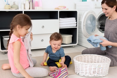Photo of Housewife with children folding freshly washed clothes in laundry room