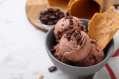 Photo of Tasty ice cream with chocolate chunks and piecewaffle cone in bowl on white table, closeup. Space for text