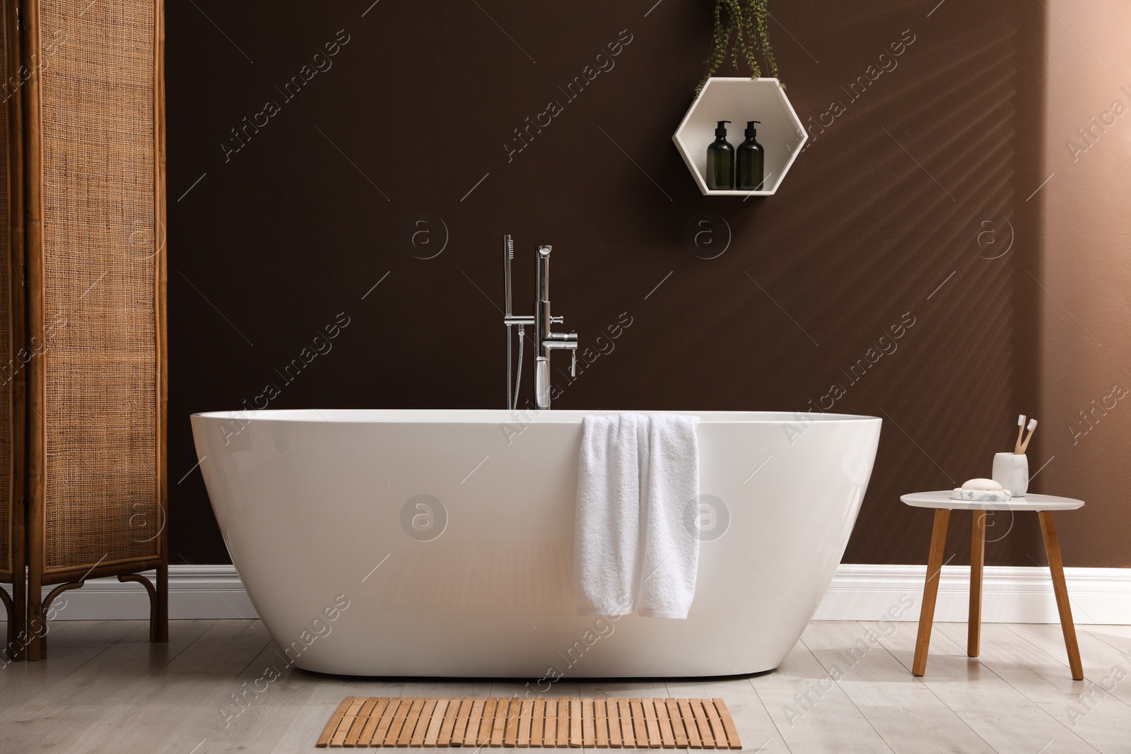Photo of Modern ceramic bathtub with towel near brown wall in room