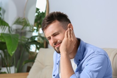 Photo of Young man suffering from ear pain at home. Space for text