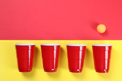 Plastic cups and ball on color background, flat lay with space for text. Beer pong game