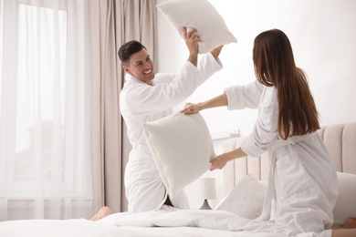 Happy couple in bathrobes having pillow fight on bed at home