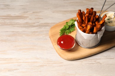 Photo of Frying basket with sweet potato fries, sauces and parsley on white wooden table. Space for text