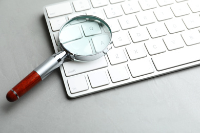 Photo of Magnifier glass and keyboard on light grey stone background, closeup. Find keywords concept