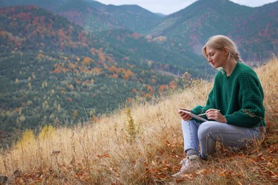 Photo of Young woman drawing on tablet in mountains, space for text