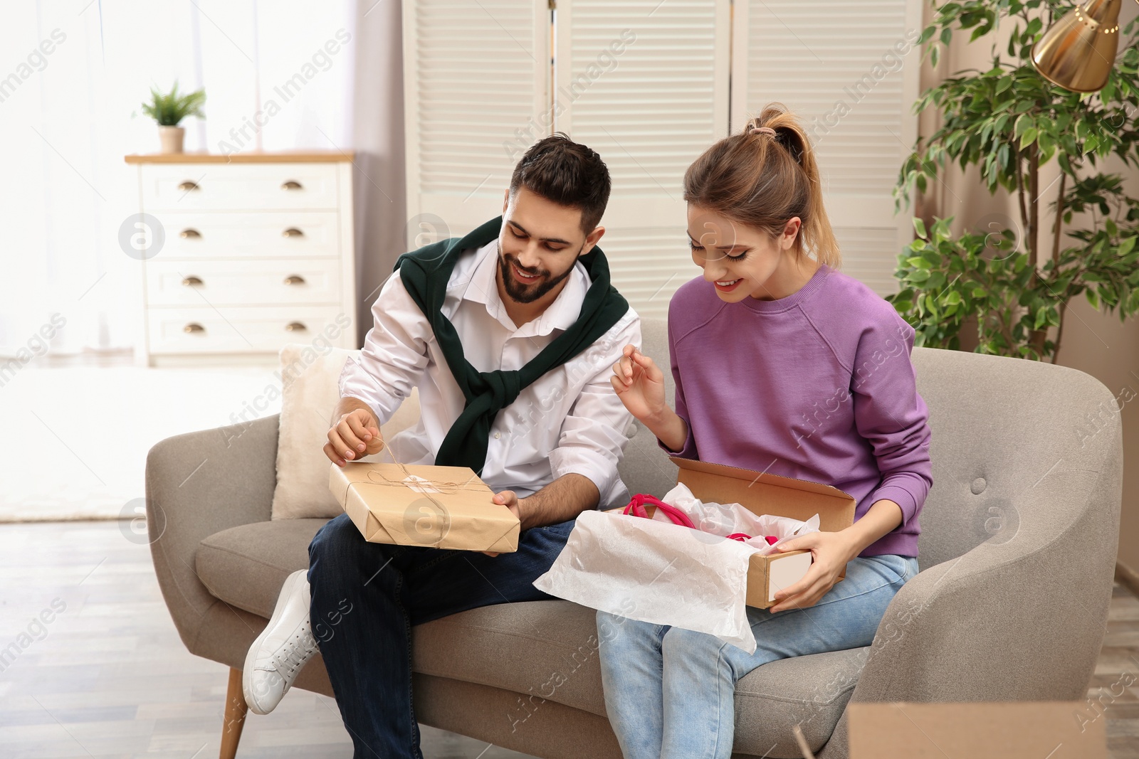 Photo of Young couple opening parcels on sofa in living room