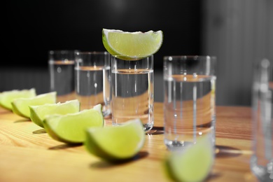 Vodka shots and lime slices on wooden bar counter, closeup