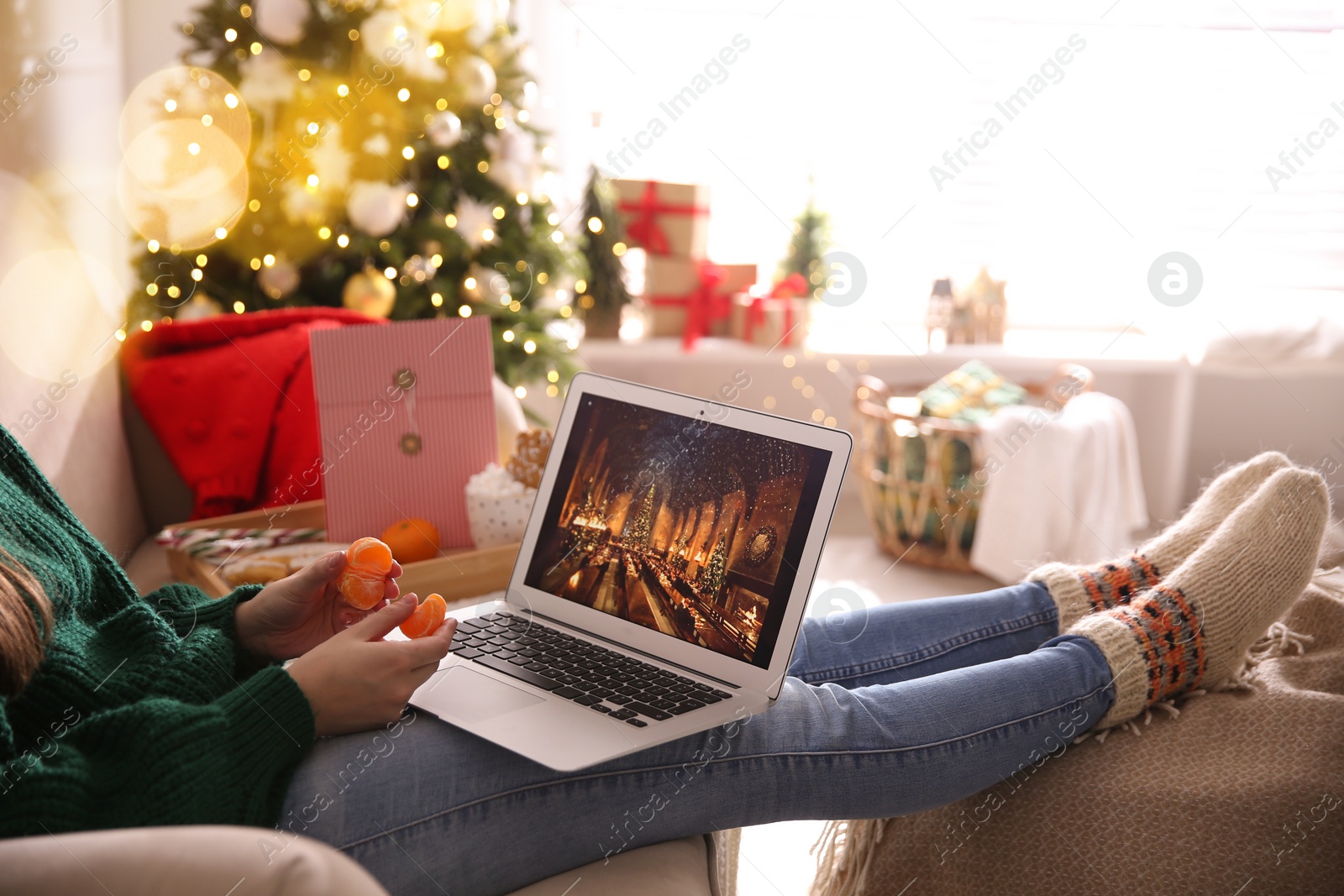 Photo of MYKOLAIV, UKRAINE - DECEMBER 25, 2020: Woman with tangerine watching Harry Potter and Philosopher's stone movie on laptop at home, closeup. Cozy winter holidays atmosphere