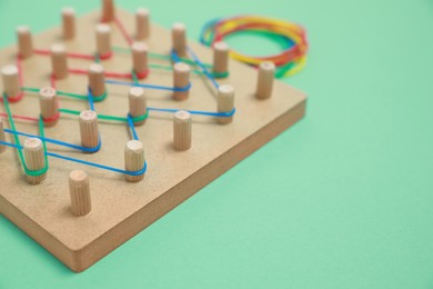 Photo of Wooden geoboard with rubber bands on green background, closeup with space for text. Educational toy for motor skills development