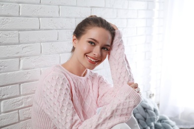 Young woman wearing knitted sweater near white brick wall