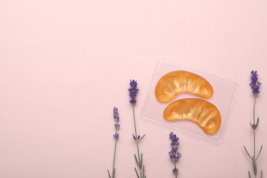 Photo of Package with under eye patches and lavender flowers on light pink background, flat lay. Space for text