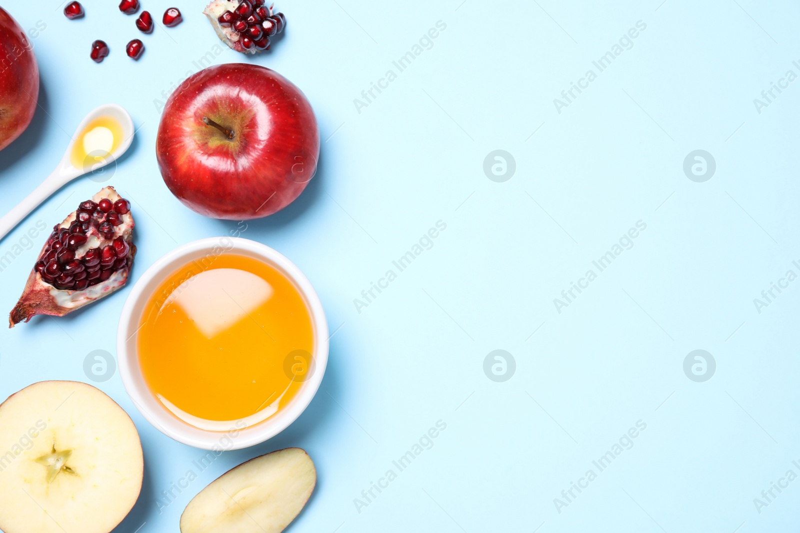 Photo of Honey, apples and pomegranates on light blue background, flat lay with space for text. Rosh Hashanah holiday