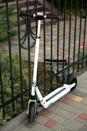Photo of Modern electric kick scooter near metal fence outdoors