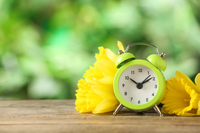 Alarm clock and beautiful spring flowers on wooden table, space for text. Time change concept