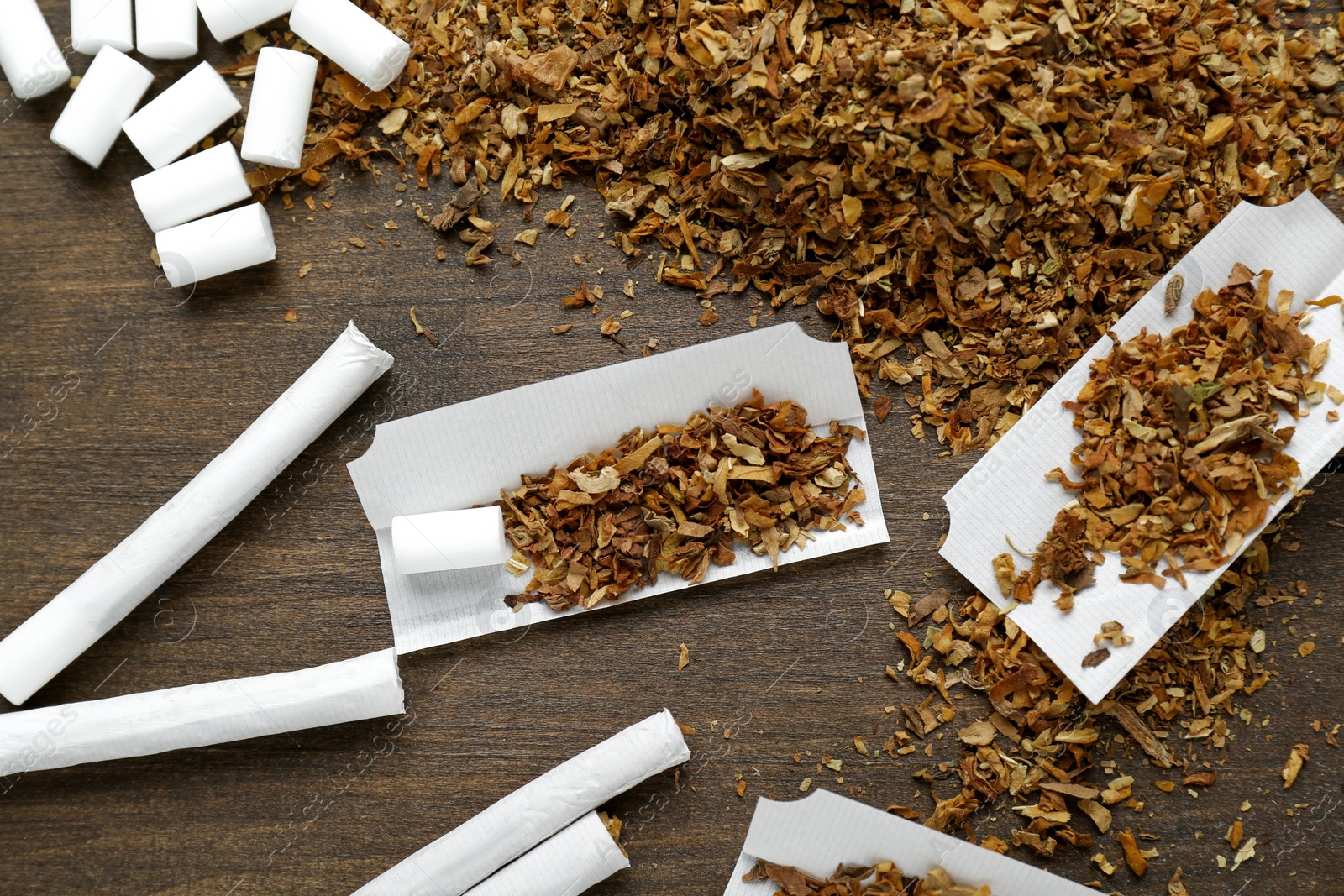 Photo of Hand rolled cigarettes, filters and tobacco on wooden table, flat lay