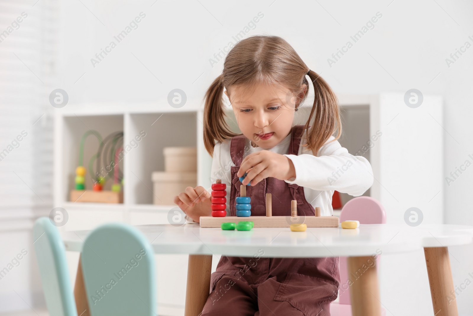 Photo of Cute little girl playing with stacking and counting game at white table indoors, space for text. Child's toy