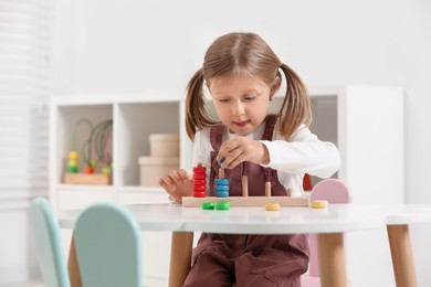 Photo of Cute little girl playing with stacking and counting game at white table indoors, space for text. Child's toy