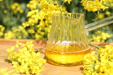 Photo of Rapeseed oil in jug and flowers on tray outdoors, closeup
