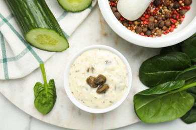 Photo of Creamy caper sauce in bowl and ingredients on marble table, flat lay