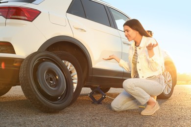 Photo of Worried young woman near car on roadside. Changing wheel